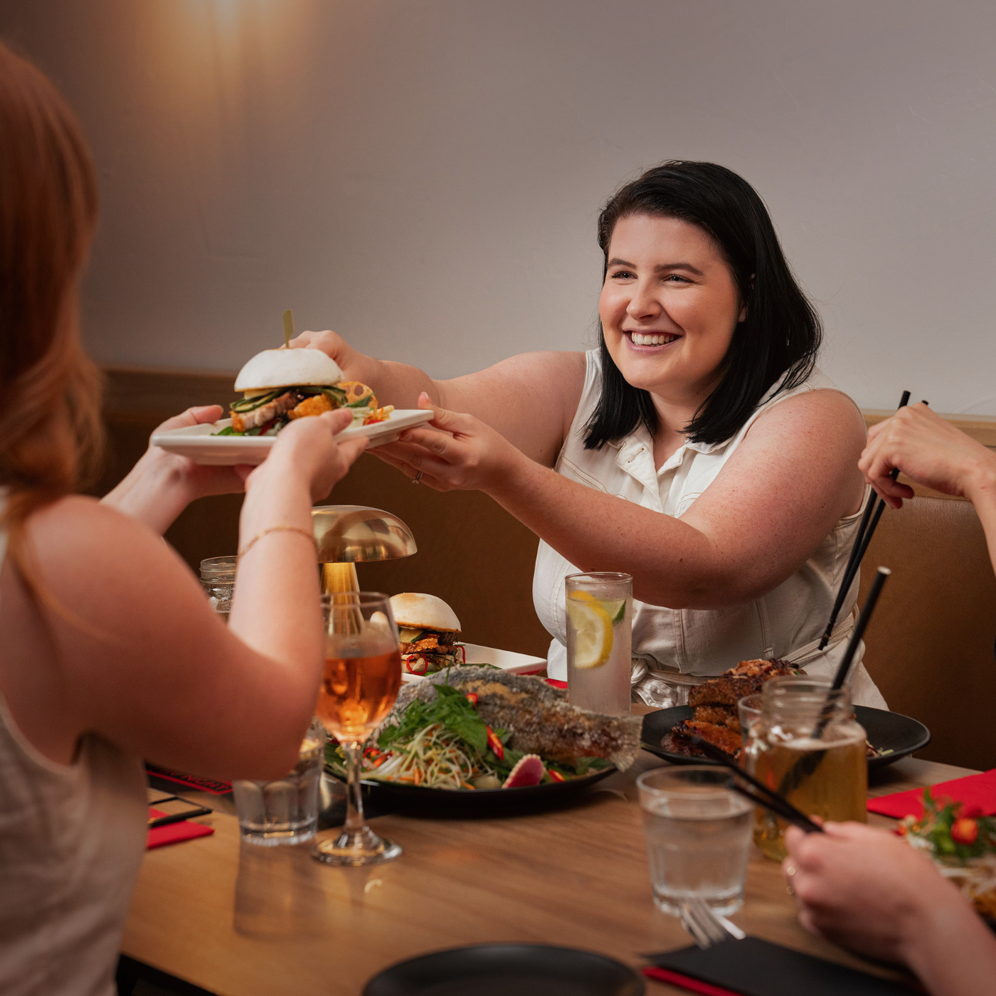 A Dark haired young woman dressed in white getting served an Asian style dish.